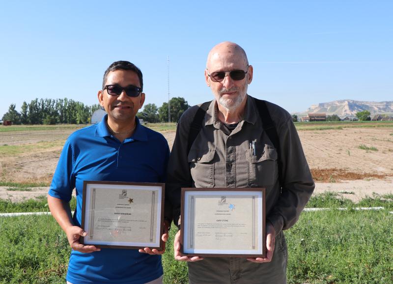 Two men hold awards outside 