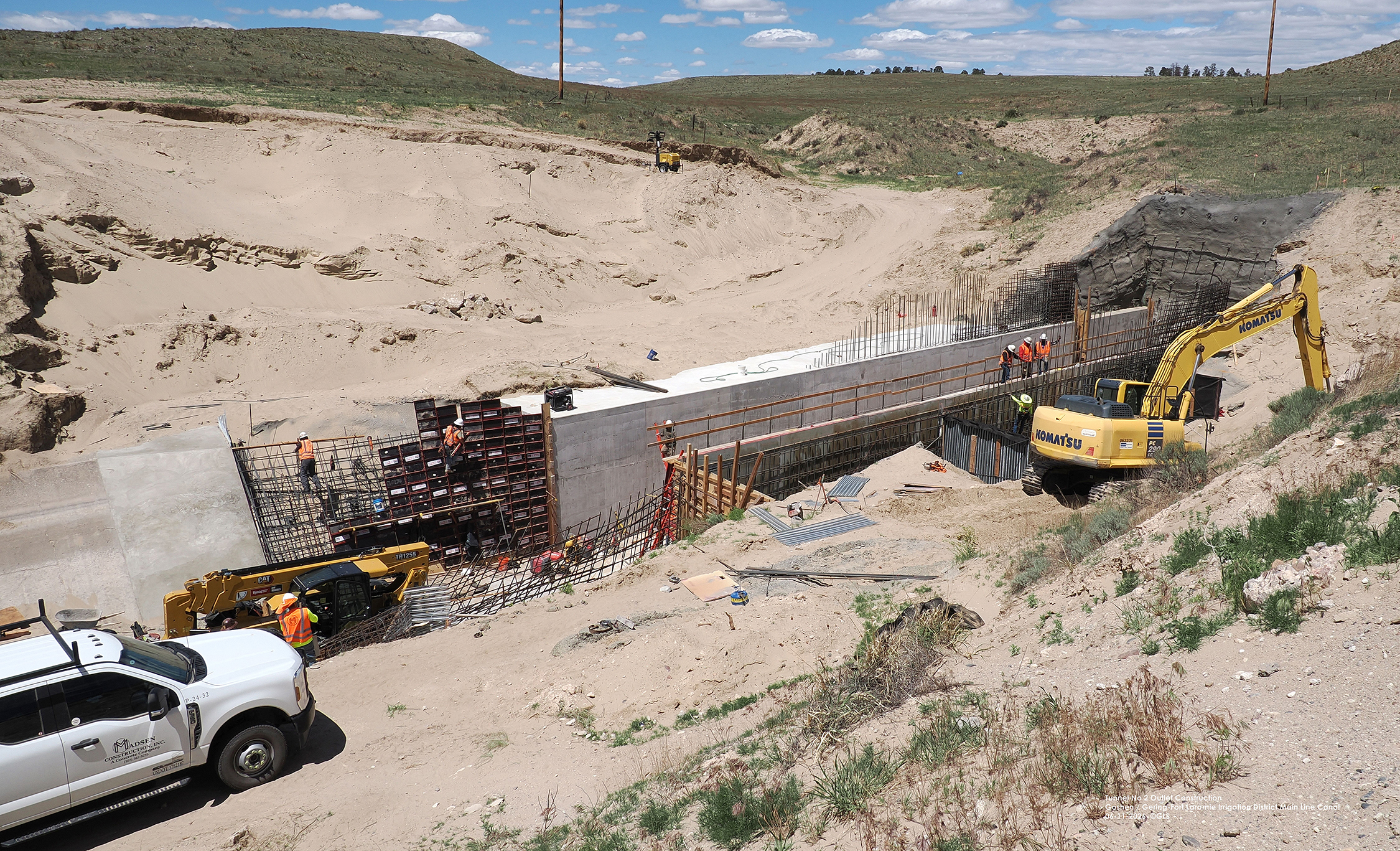 Construction site with workers, vehicles, and machinery building a structure in a sandy area.