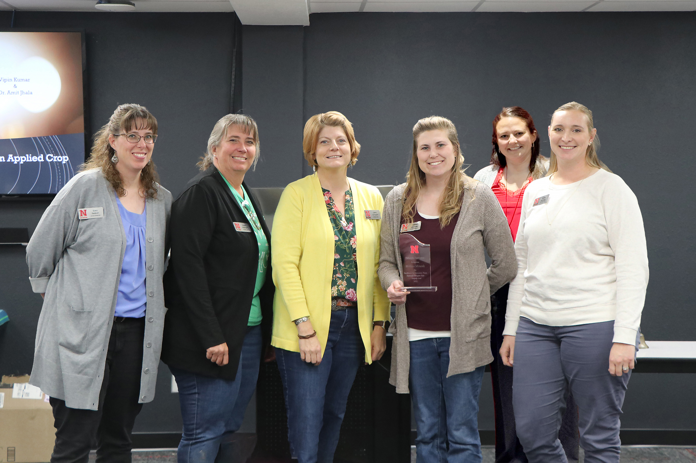 Group of six adults standing in a room with a plaque, one person holding a clear award.