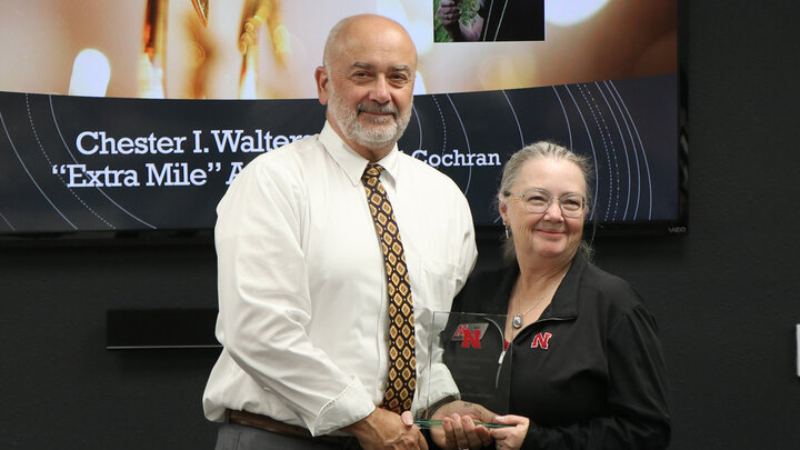 Two people standing together, holding an award in a formal indoor setting.
