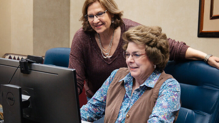 two women sit in front of computer