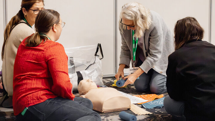 four women sit around a CPR dummy at a training 