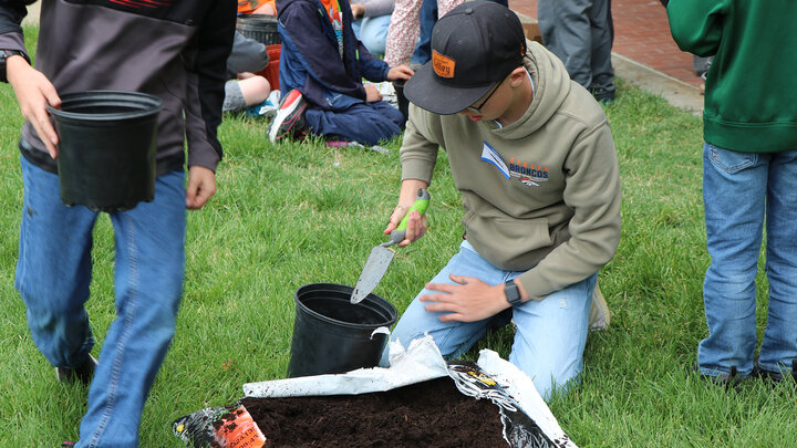 Boy puts dirt in pot sitting on grass