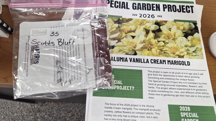Plastic bag labeled "Scotts Bluff" next to a gardening project flyer featuring yellow marigold flowers.