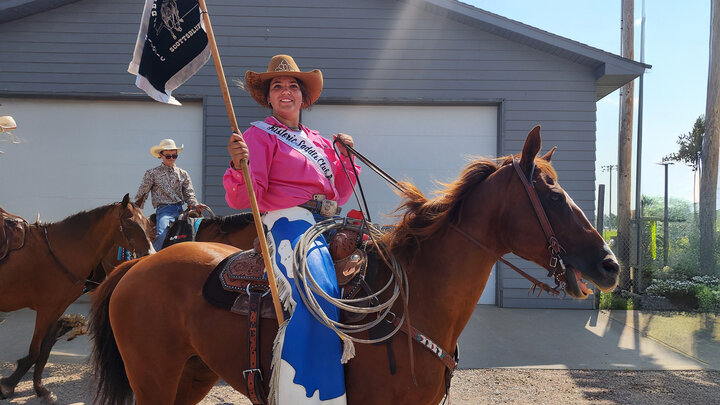 Cowgirl with flag and chaps on horse before entering arena