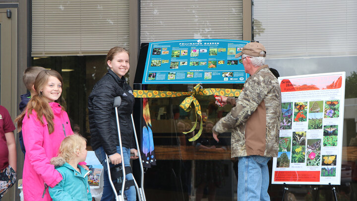 three girls and a man cut ribbon on plaque at ceremony