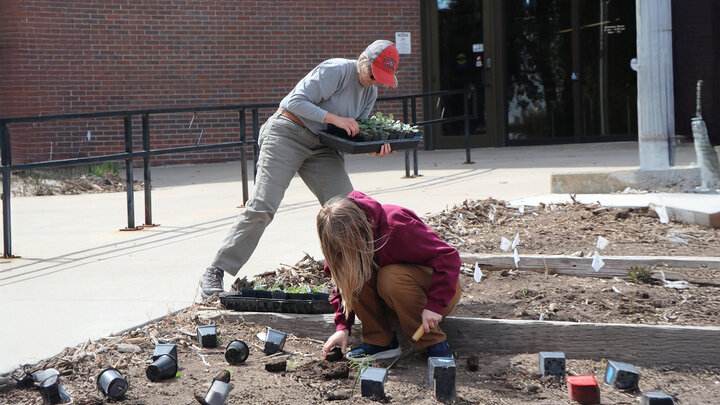 two women plant flowers outside of community building