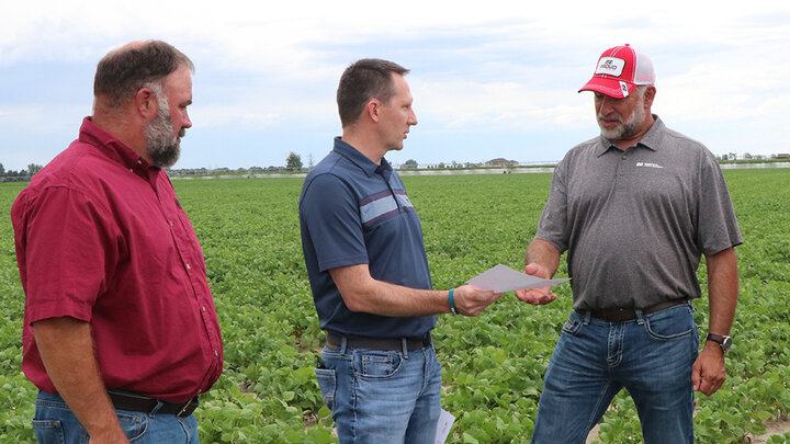 two men receive check from another man in dry bean field