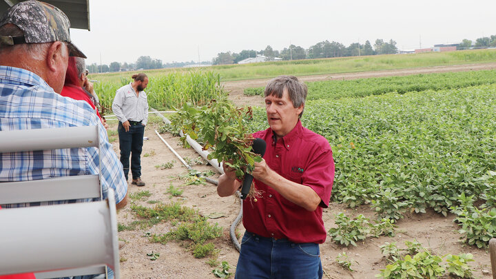 man holds up plant on field tour for people to see