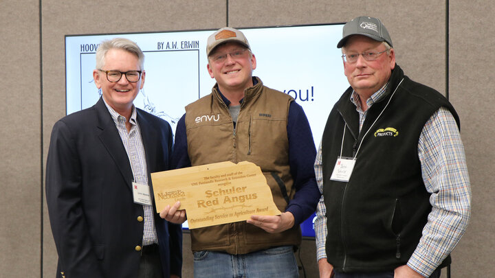 three men and center man holds plaque for award