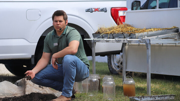 man kneels while talking to crowd at water an soil demonstration