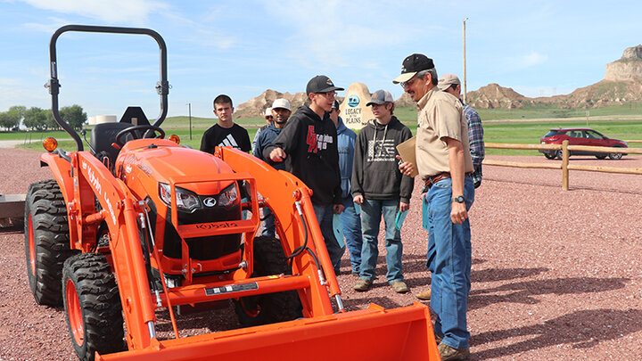 man with high schoolers discuss safety outside with tractor