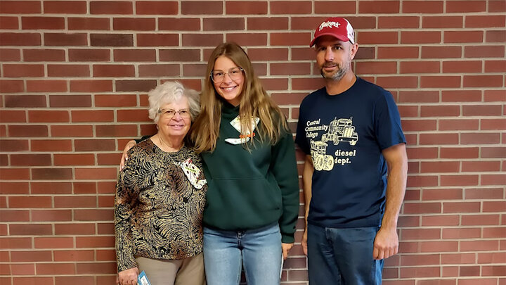 Three people standing together in front of a red brick wall.